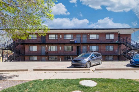 A silver car is parked in front of a red brick apartment building.