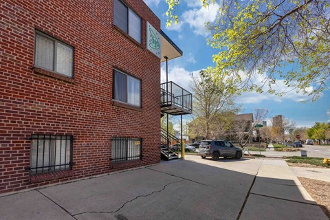 A red brick building with a balcony and a tree with yellow flowers in front.