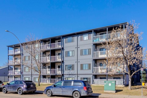 Two cars are parked in front of a grey apartment building.