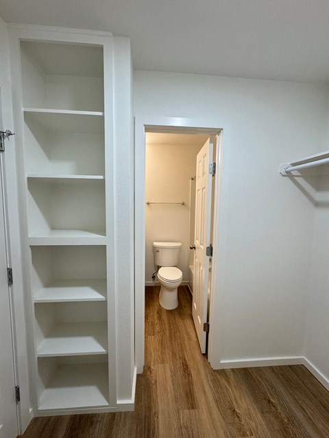 A white cabinet with shelves is open in a room with a toilet in the background.