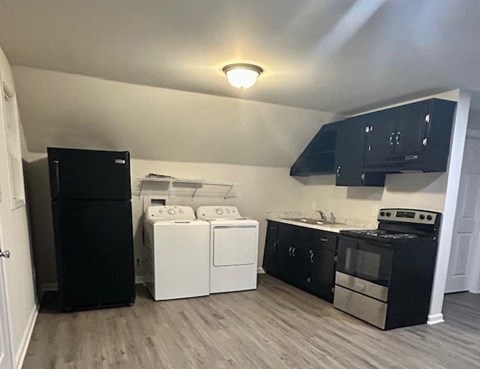 A black refrigerator is in a kitchen with black cabinets and a white washer and dryer.
