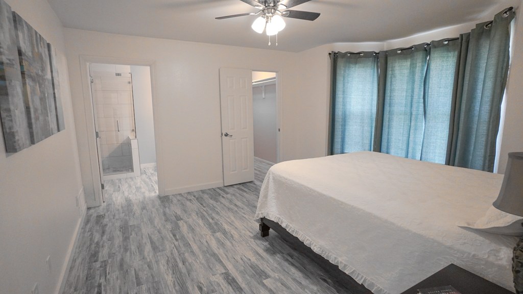 A bedroom with a bed, a ceiling fan, and a window with curtains.