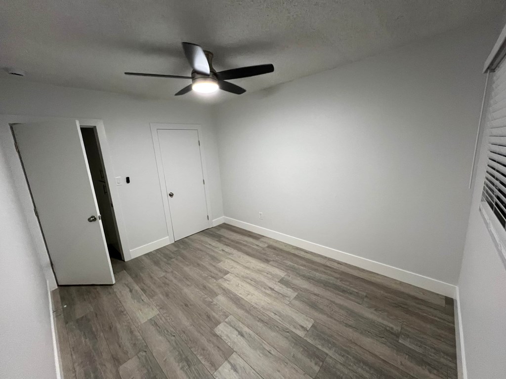 A room with a ceiling fan and wood flooring.