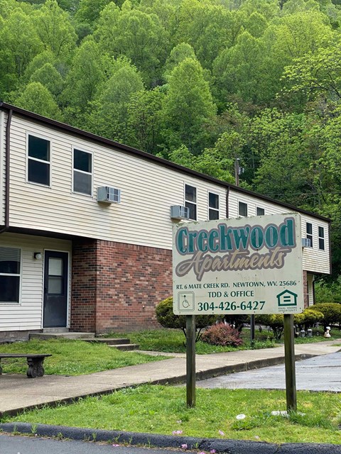 A building with a sign that says "Creekwood Apartments" in front of a forest.