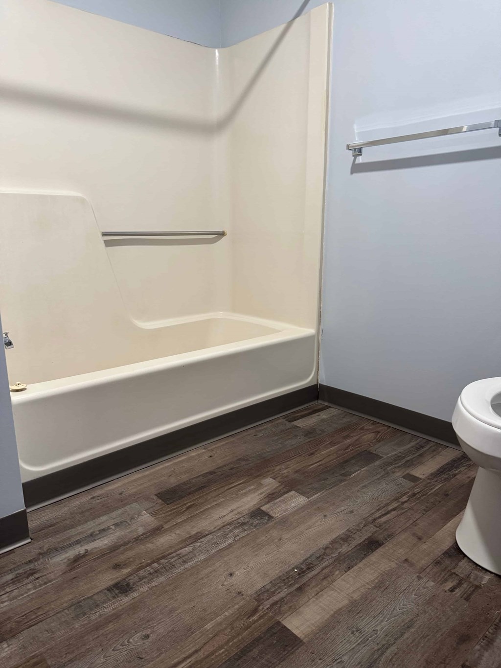 A white toilet sits in a bathroom with wood flooring and white walls.