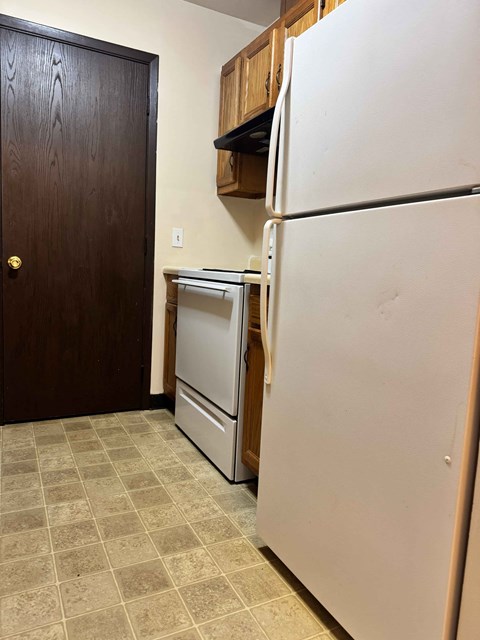 A white refrigerator stands in a kitchen next to a wooden door.