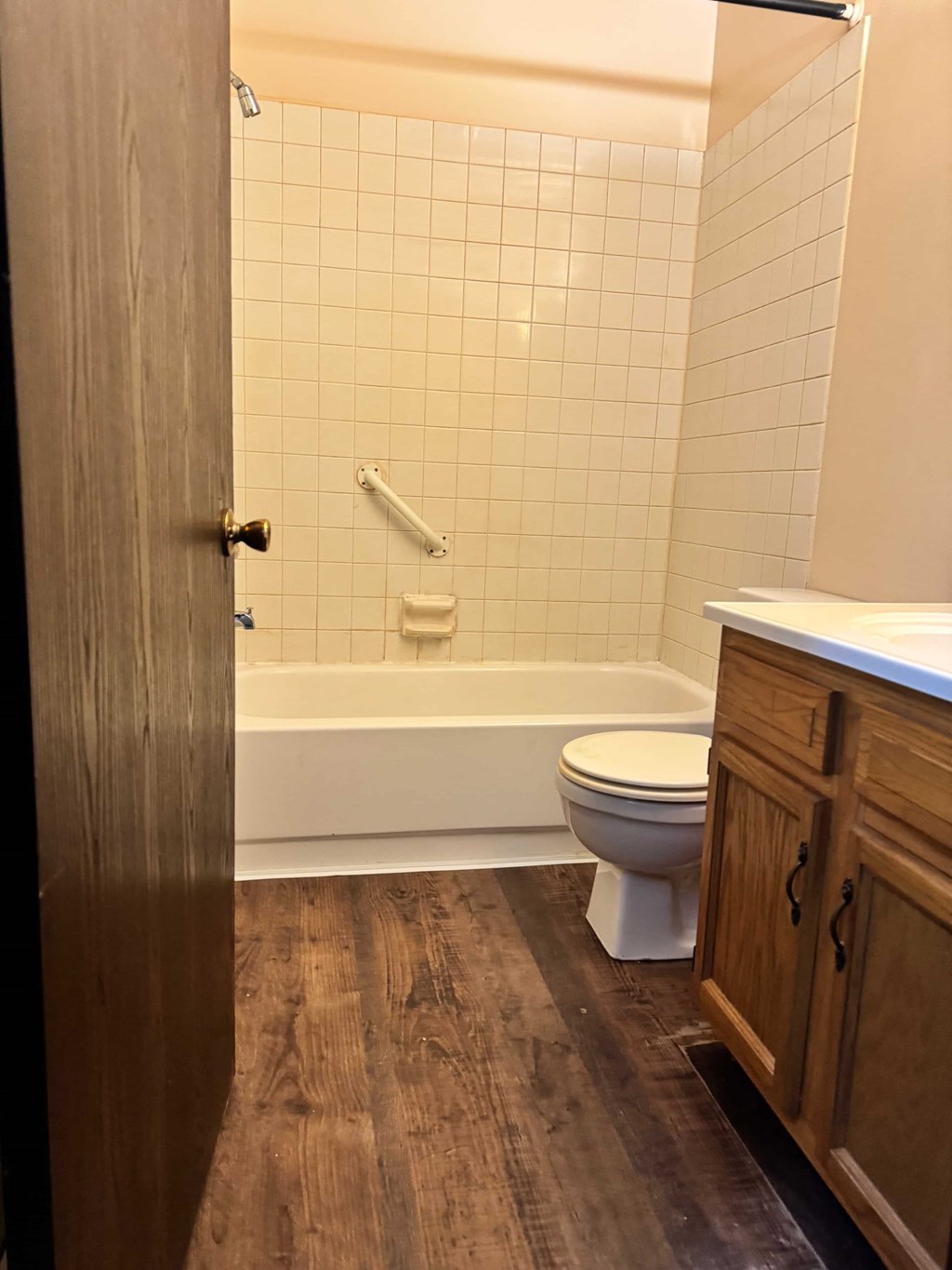 A white toilet sits in a bathroom with a wooden floor and a white tiled shower.