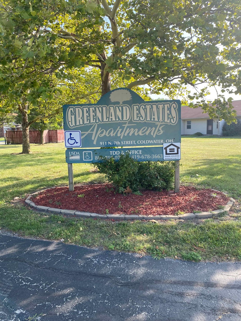 A sign for Greenland Estates Apartments is in front of a tree.