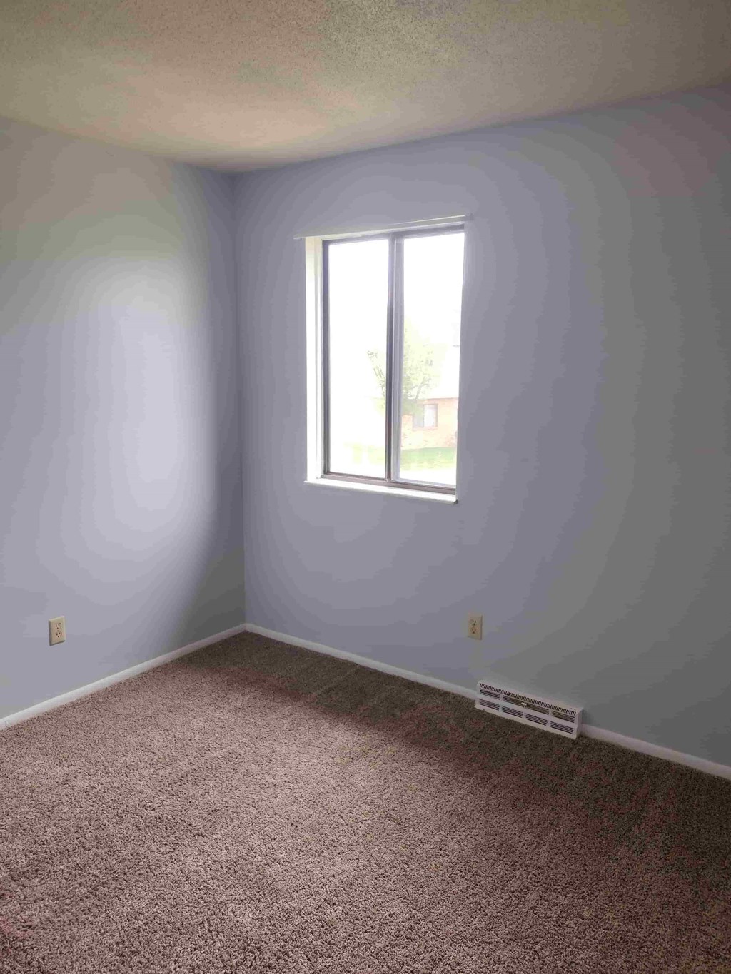 A room with a window and a carpeted floor.
