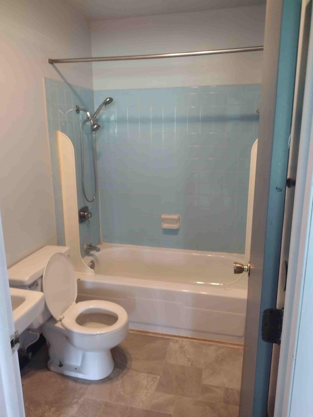 A white toilet sits in a bathroom with a blue tiled shower.