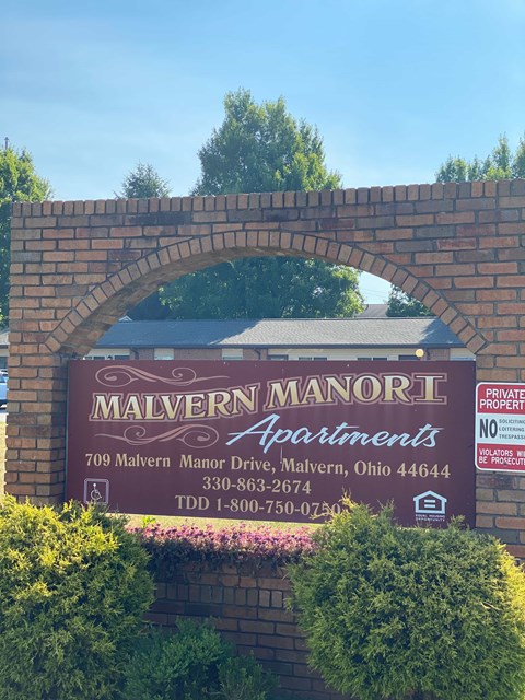 A sign for Malvern Manor Apartments is displayed on a brick wall.