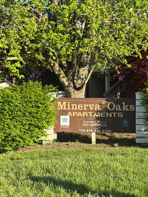 A sign for Minerva Oaks Apartments stands in front of a tree.