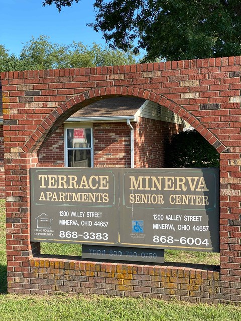 A sign for Terrace Apartments and Minerva Senior Center is displayed on a brick wall.