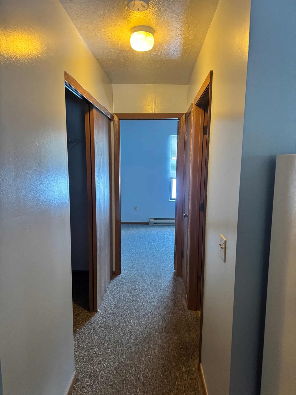 A hallway with a carpeted floor and a light on the ceiling.
