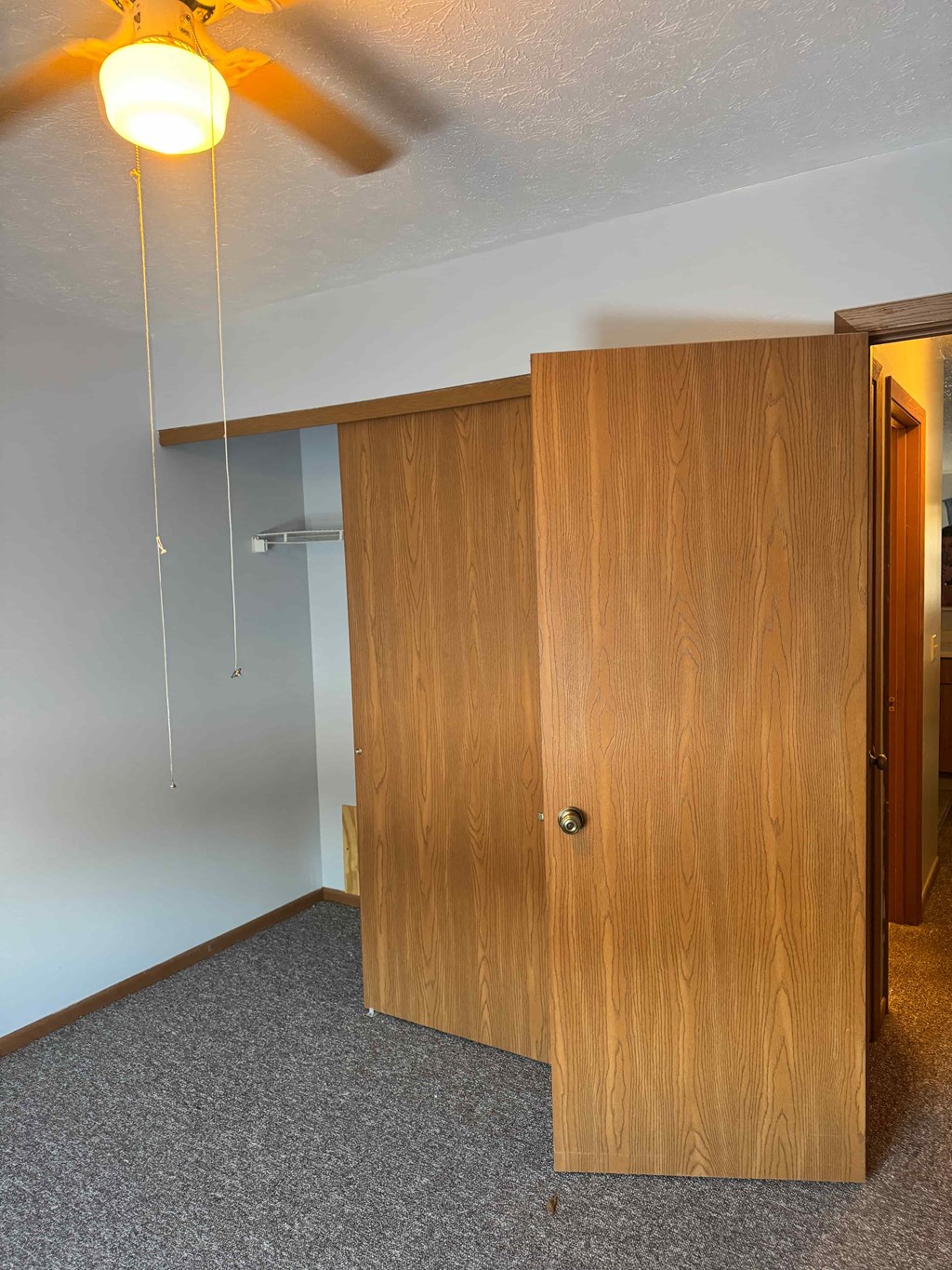 A wooden door with a silver handle is in a room with a ceiling fan.
