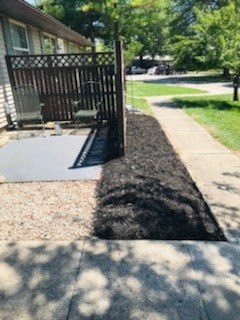 A black dog is standing on a sidewalk.