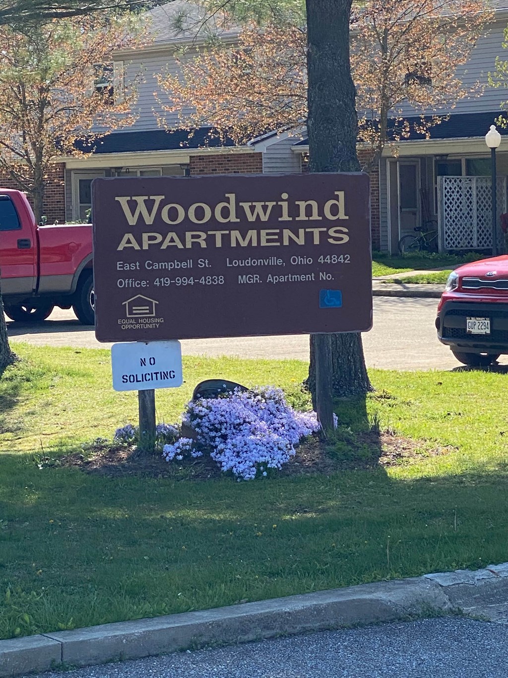 A sign for Woodwind Apartments is displayed in front of a tree.