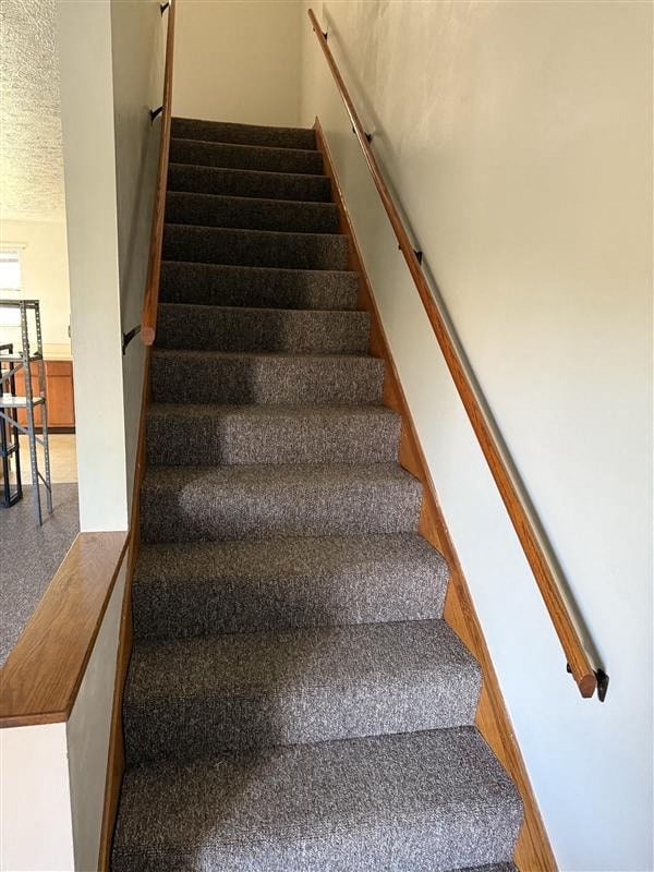 A staircase with a wooden handrail and grey carpeted steps.