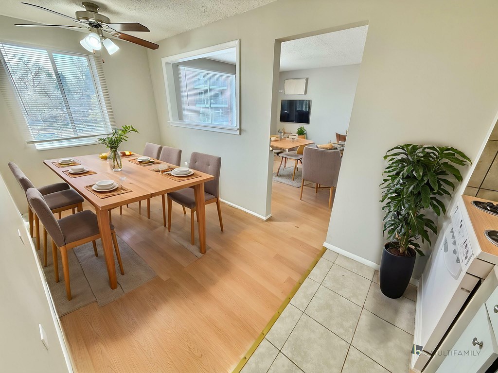 A dining room with a table set for six with a plant on the side.