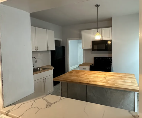 A kitchen with a black fridge and microwave, a wooden counter top, and white cabinets.