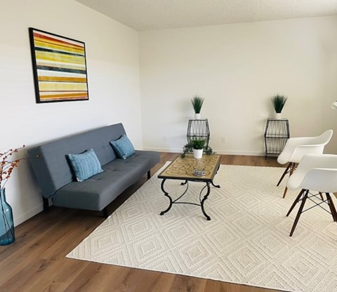 A living room with a grey couch, a coffee table, and two white chairs.