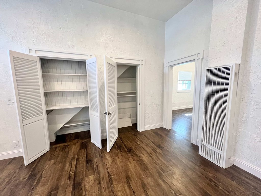 A room with white walls and wooden flooring, featuring a built-in pantry with open doors.