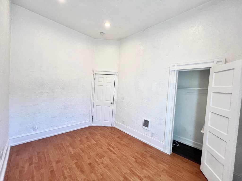 A room with wooden floors and white walls, with a door and a window.