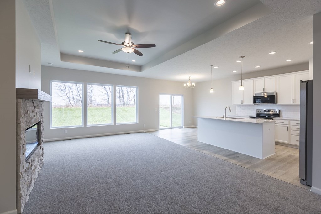 A spacious living room with a ceiling fan and a kitchen area in the background.