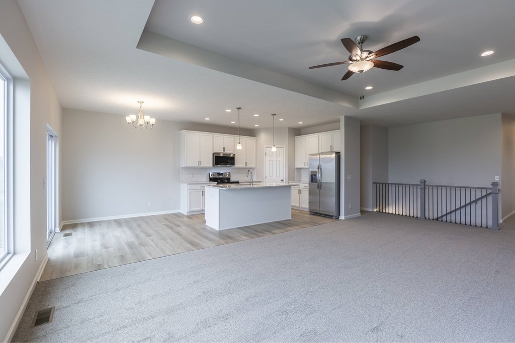 A spacious, empty room with a ceiling fan and a kitchen area in the background.