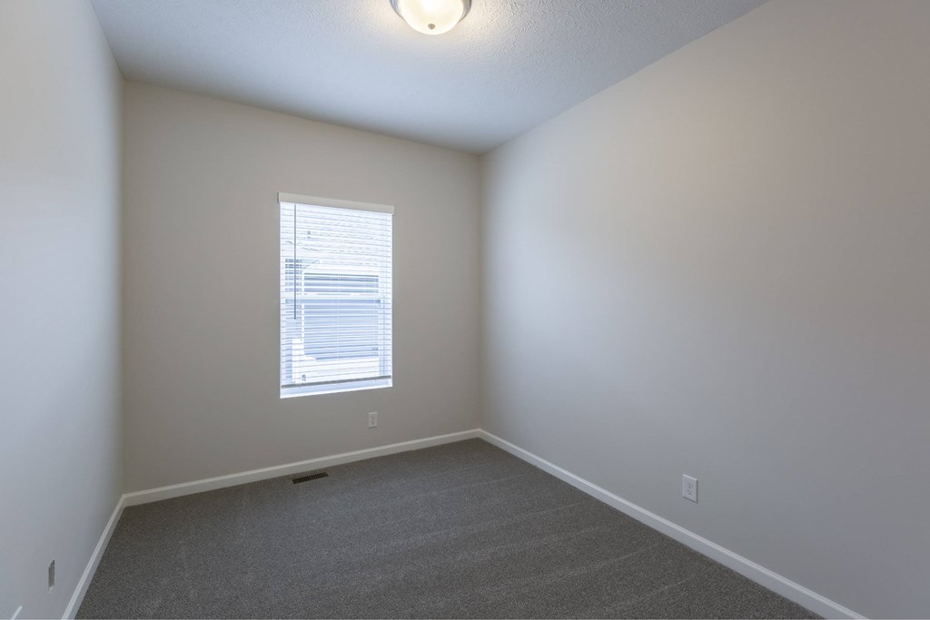 A room with a carpeted floor and a window with blinds.
