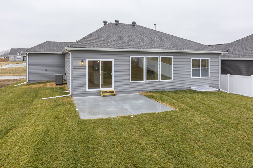 A grey house with a concrete patio and a white fence.