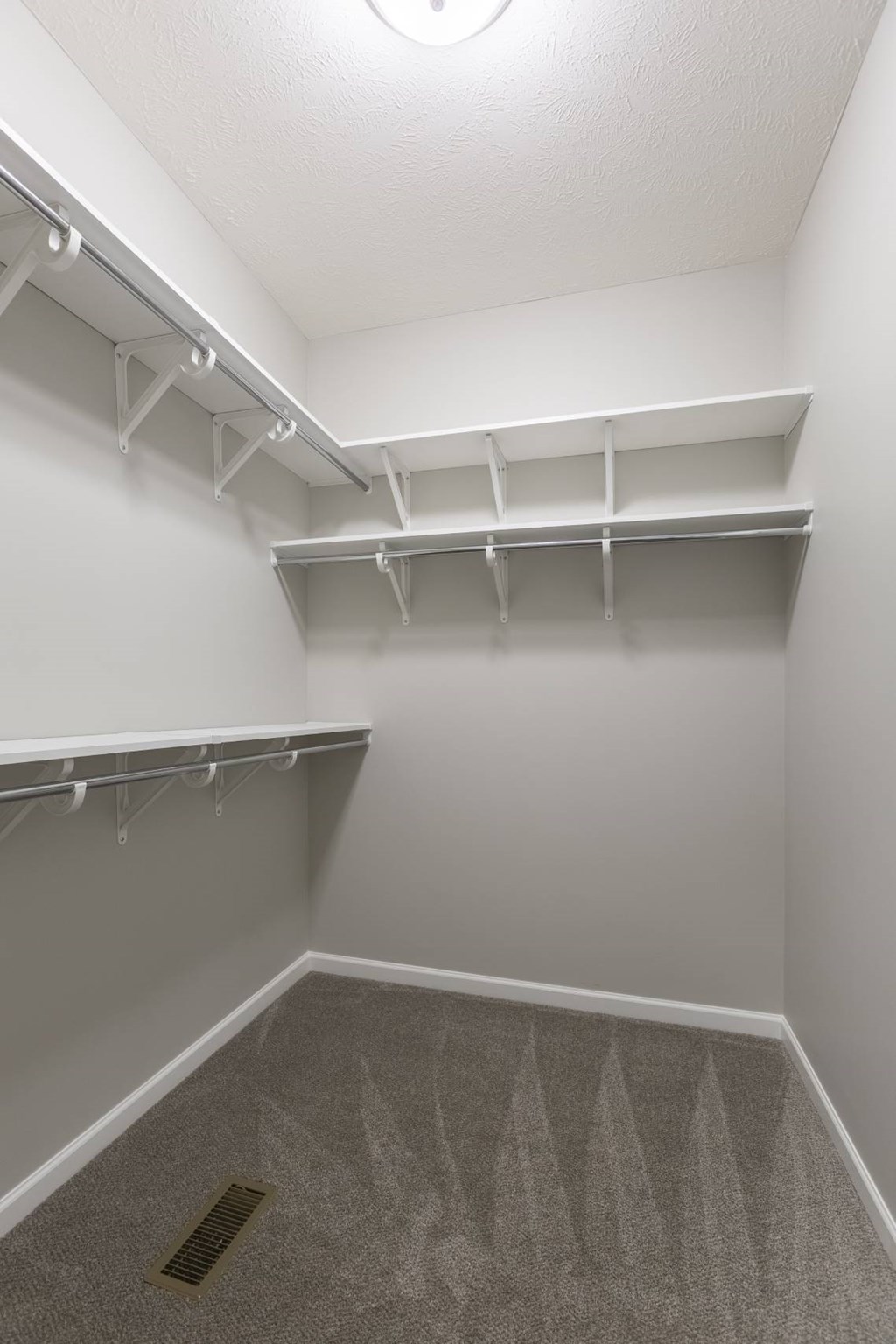 A white closet with a carpeted floor and a vent in the ceiling.