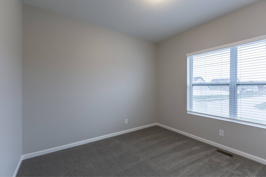 A room with a carpeted floor and a window with blinds.