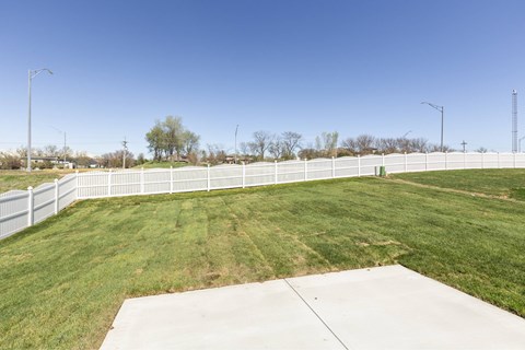 A large, open grassy area with a white fence and a concrete pathway.