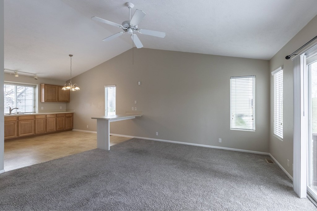 A spacious room with a grey carpet and a ceiling fan.
