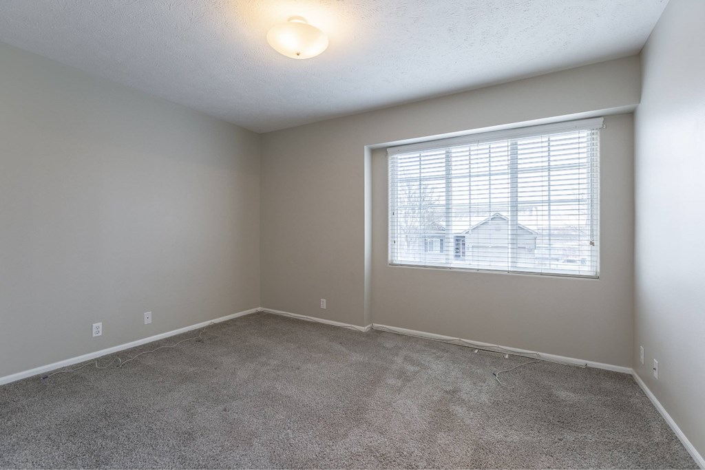 A room with a carpeted floor and a window with blinds.