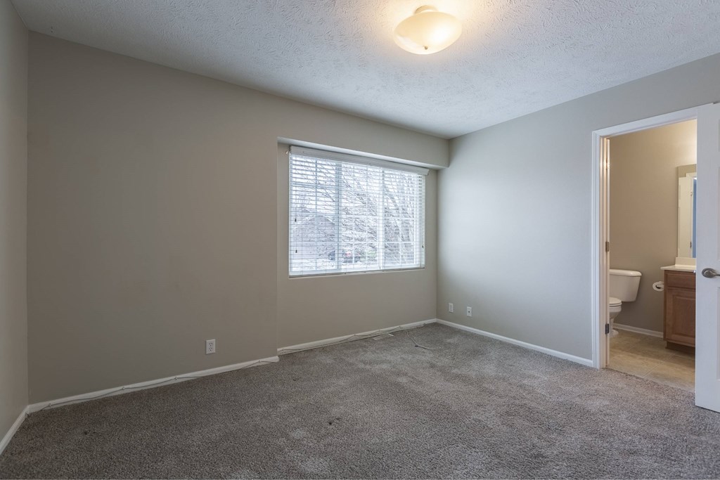 A room with a carpeted floor and a window with blinds.