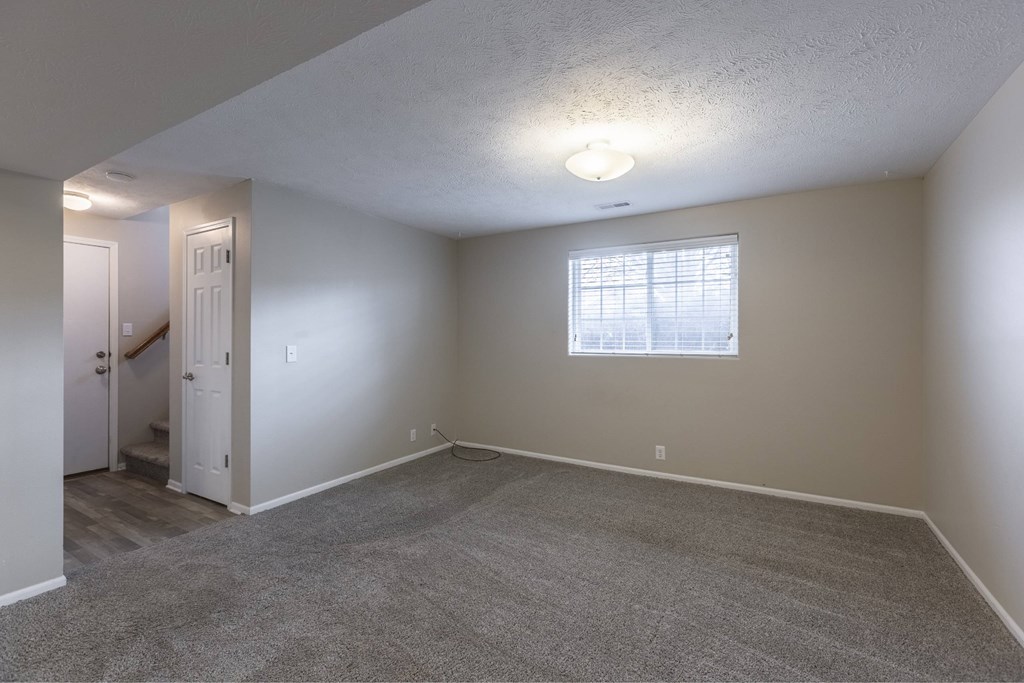 A room with a carpeted floor and a window with blinds.