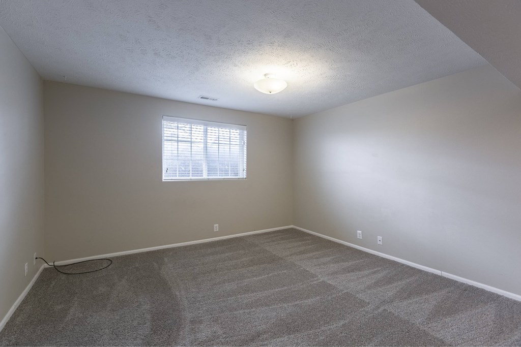 A room with a carpeted floor and a window with blinds.