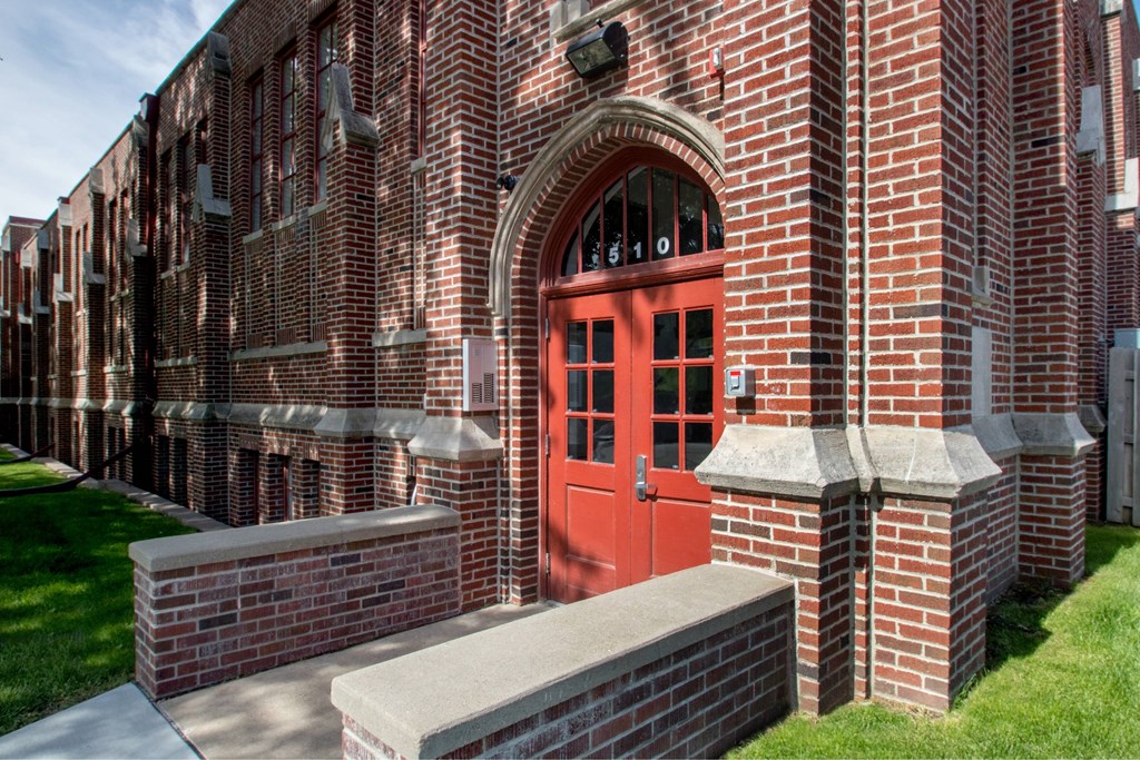 A red door is on the side of a brick building.