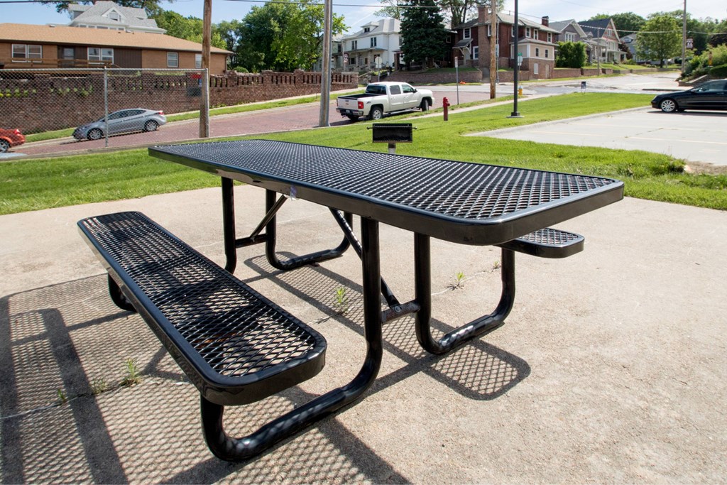 A black picnic table and bench are in the foreground of a sunny day.