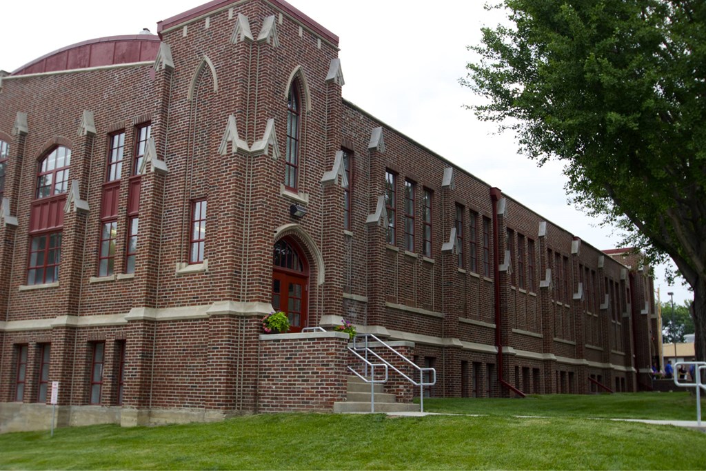 A red brick building with a large arched doorway and a staircase leading to the entrance.