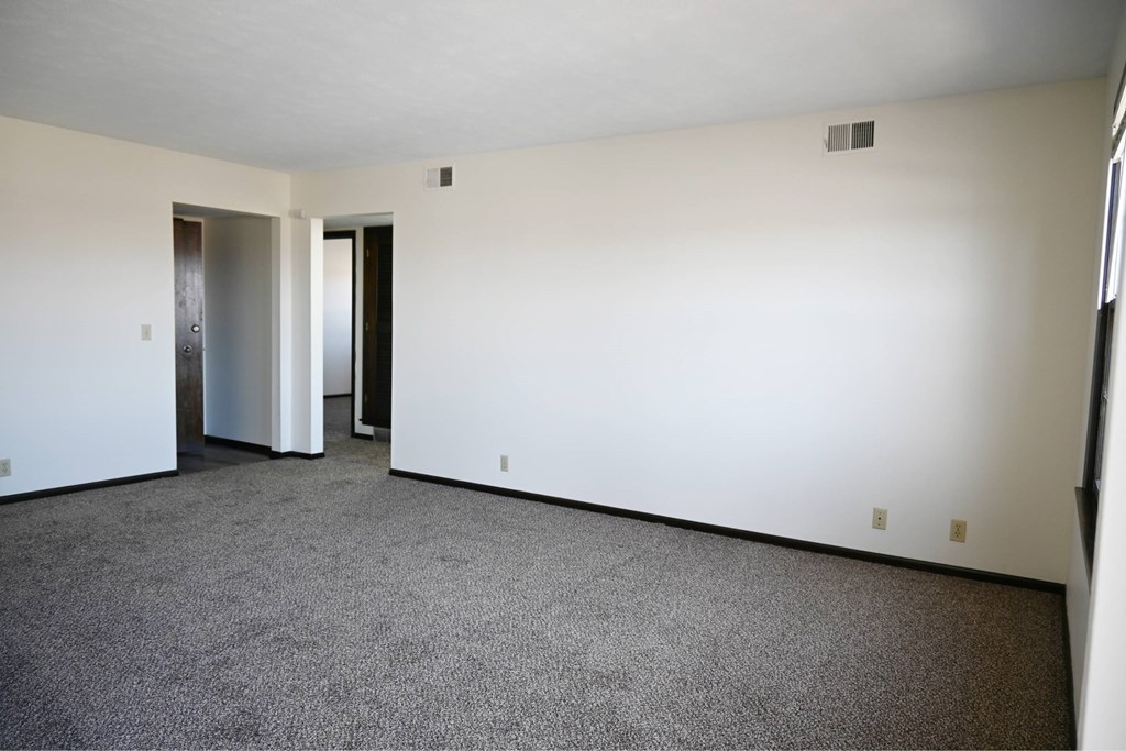 A large empty room with a carpeted floor and two doors.
