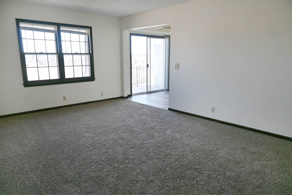 A room with a carpeted floor, a window, and a sliding glass door.