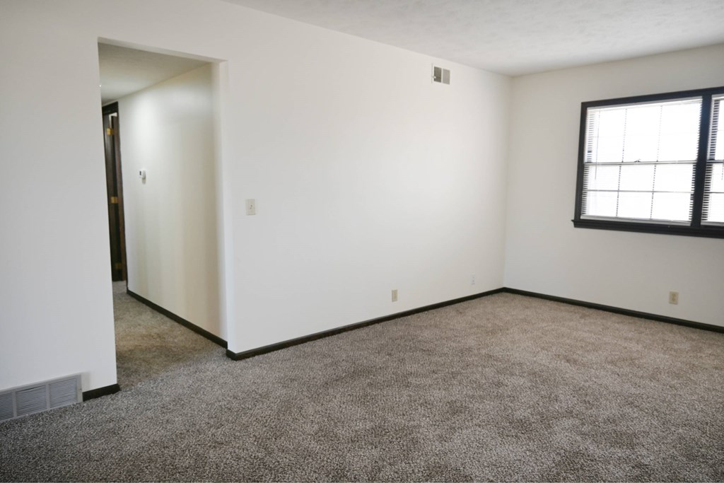 A room with a carpeted floor and a window with blinds.