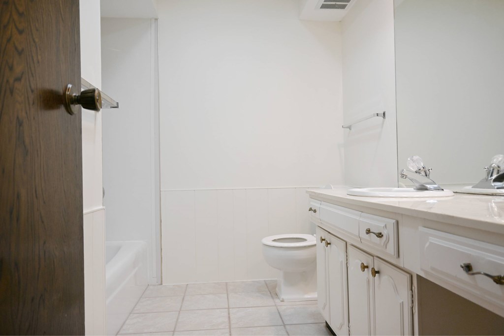 A white bathroom with a toilet, sink, and a wooden door.