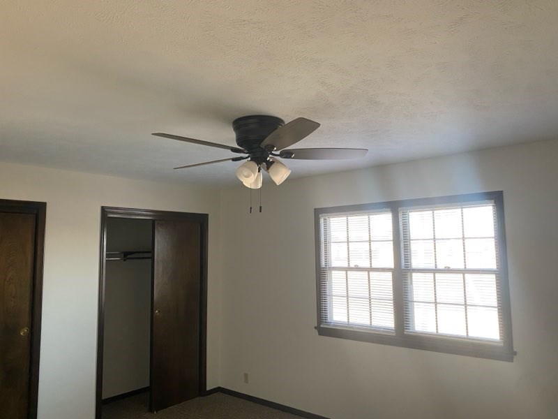 A room with a ceiling fan and a window with blinds.