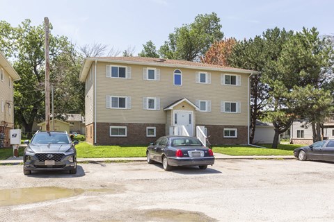 A two-story building with a beige exterior and a brown roof is surrounded by parked cars.