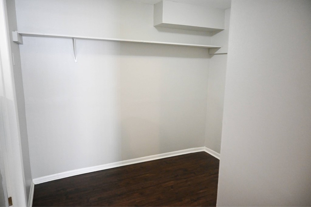 A white wall with a shelf and a brown floor.