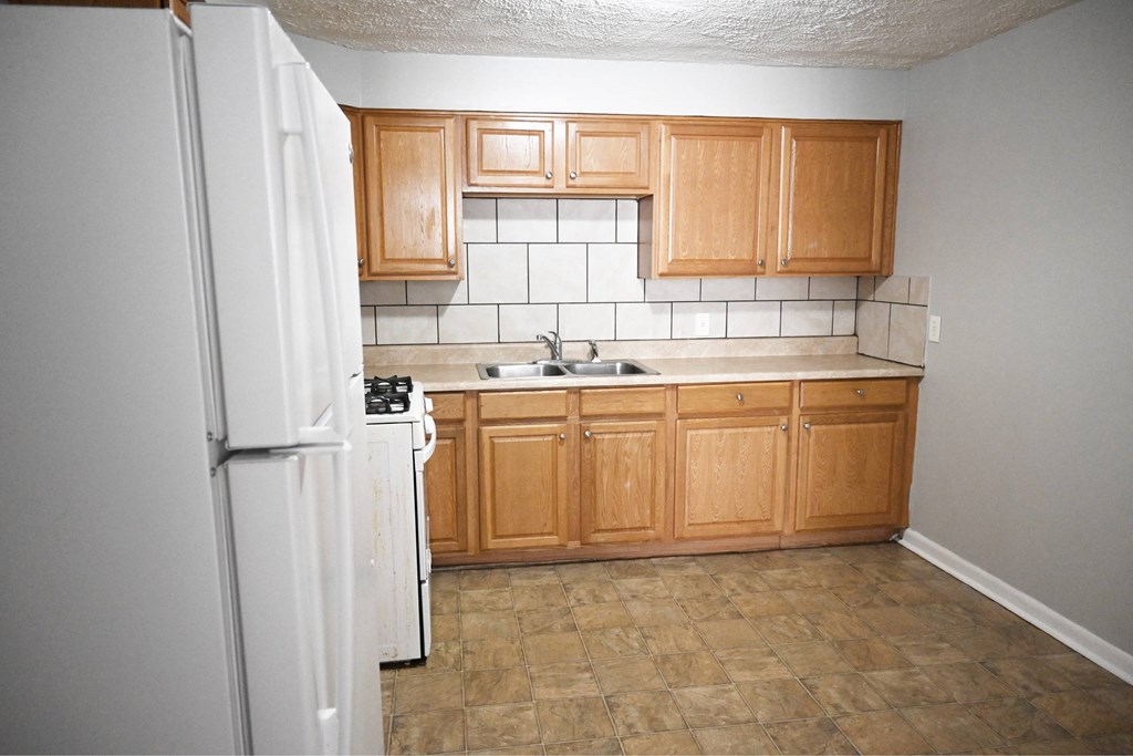A kitchen with a white refrigerator, wooden cabinets, and a tiled backsplash.